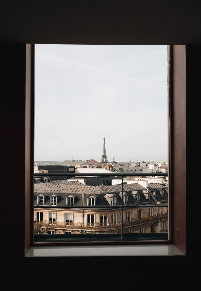Blick durch ein dunkles Fenster auf Pariser Dächer und den Eiffelturm