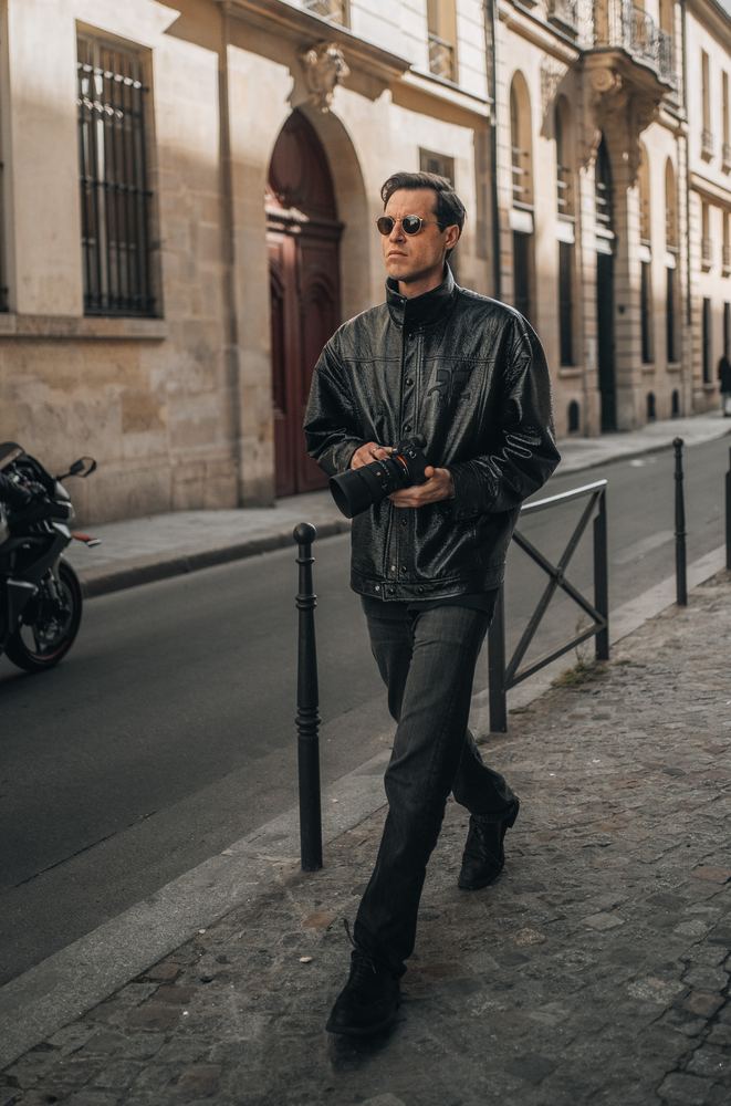 Mann in Lederjacke und Sonnenbrille läuft über einen Gehweg