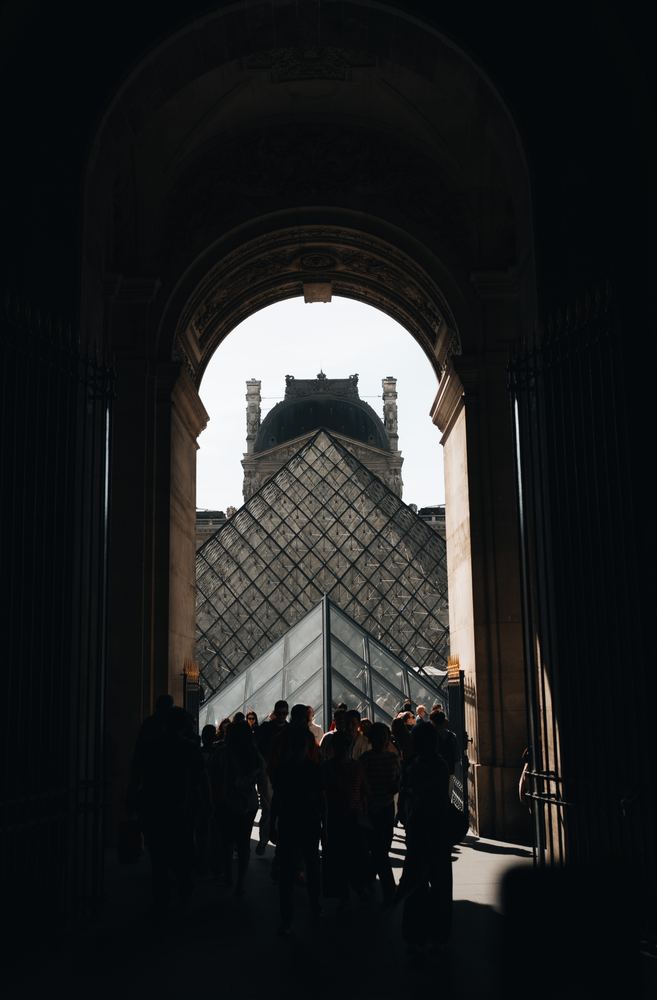 Durchgang mit Silhouetten, dahinter die Glaspyramide des Louvre