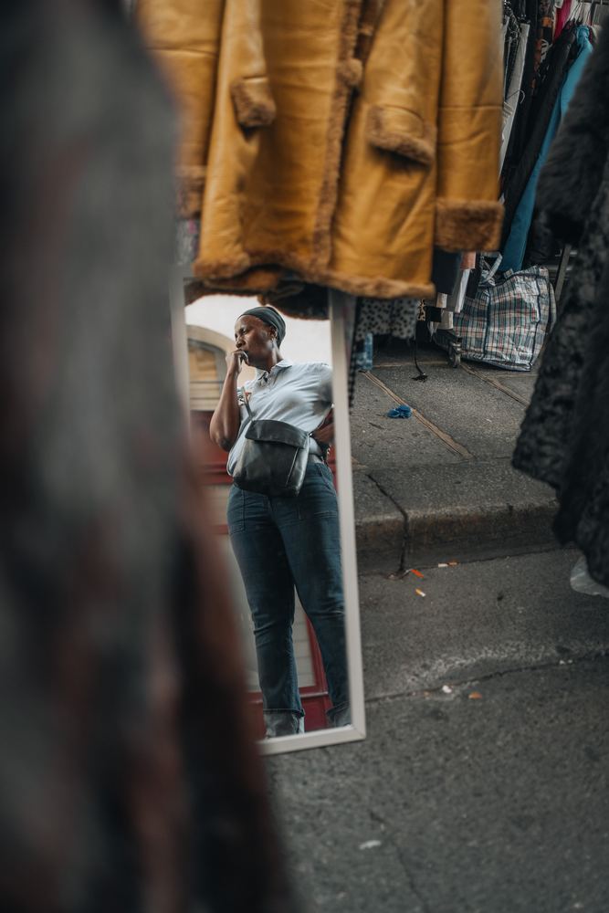 Frau in einem Spiegel zwischen Mänteln auf einem Flohmarkt