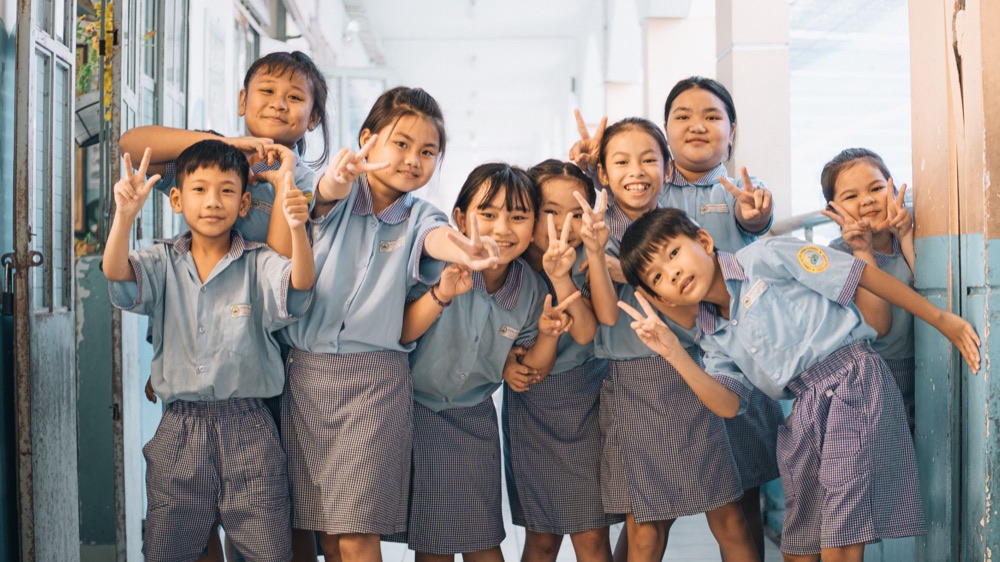 Schulkinder in Uniform machen Peace-Zeichen im Flur